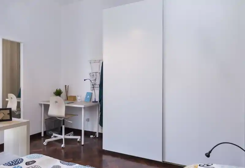 Bright, modern bedroom with a visible bed corner, clean white wardrobe and a small study desk—ideal for guests or students.