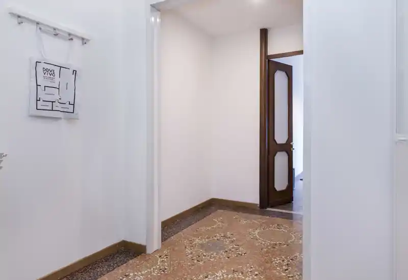 Bright, minimal entrance hallway with decorative terrazzo flooring, white walls and a wooden interior door leading to the next room.