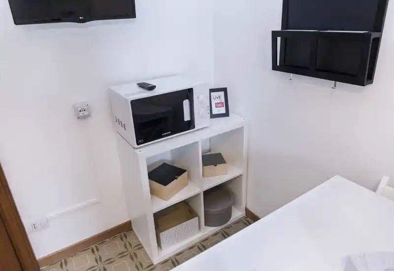 Angolo cucina compatto con microonde su un piccolo scaffale, scatole portaoggetti decorative e TV a muro — pratico e luminoso, ideale per soggiorni brevi.
