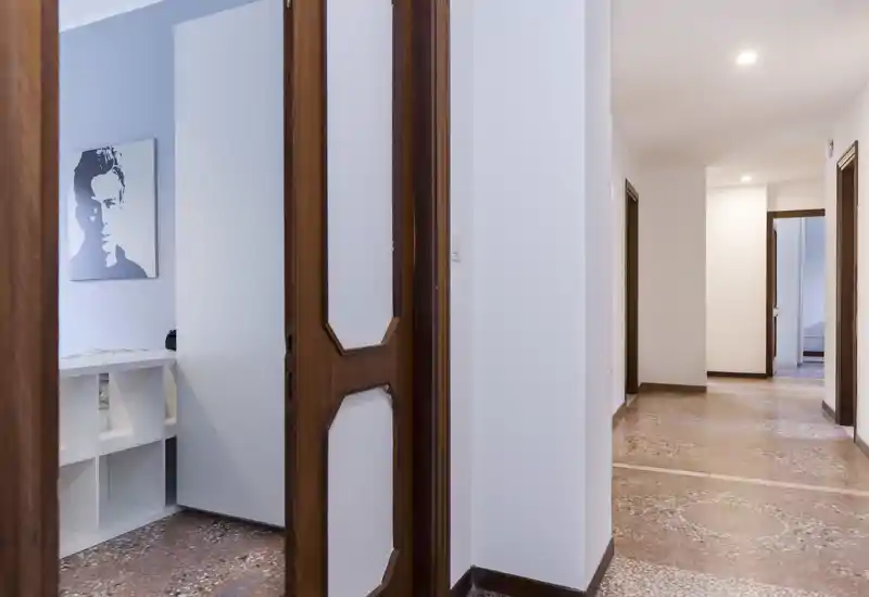 Bright, clean entrance hallway with terrazzo flooring and wooden doors, leading to several rooms — ideal as a welcoming foyer.