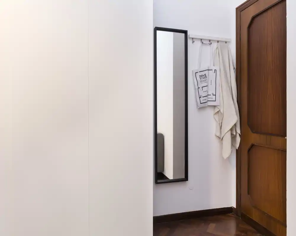 Piccolo ingresso ordinato con specchio a figura intera, appendiabiti con tessili e porta in legno; stile minimal pulito, adatto a annunci di appartamento.