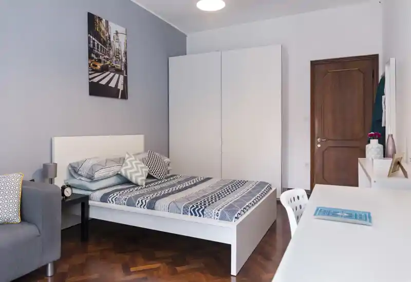 Dormitorio moderno y luminoso con cama doble, ropa de cama estampada, armario y un pequeño escritorio — ordenado y acogedor.