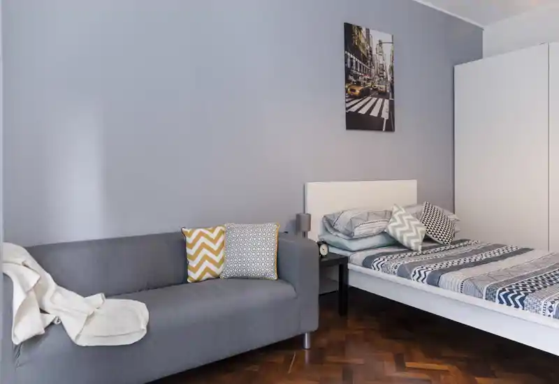 Dormitorio luminoso y moderno con cama individual, textiles estampados y un sofá compacto — bien decorado y acogedor para estancias cortas.