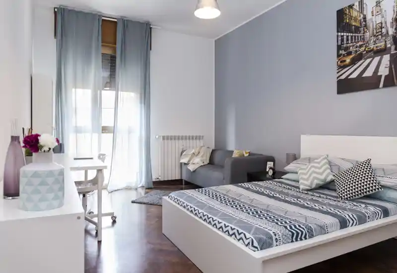 Dormitorio moderno y luminoso con cama doble, pequeño sofá y escritorio junto a la ventana — ideal para estancias cómodas y teletrabajo.