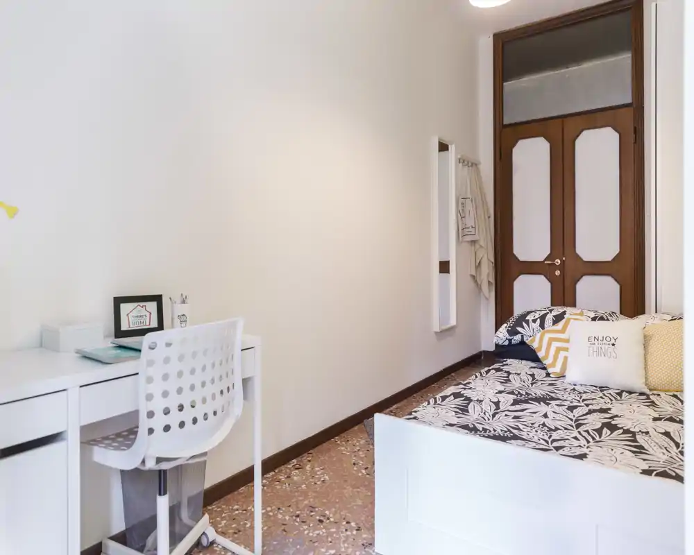 Chambre lumineuse et soignée avec lit à motifs, coussins décoratifs et petit bureau blanc — parfaite pour une location accueillante.