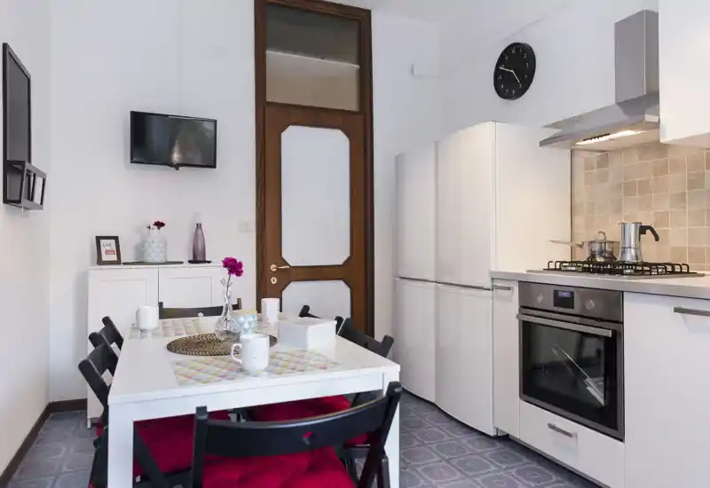 Well-equipped kitchen with a dining table for four, modern appliances and cozy red seat cushions — bright, clean and ready for meals.