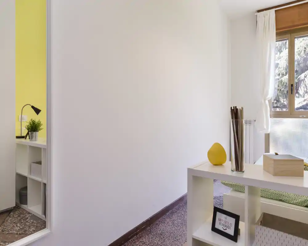 Compact, bright bedroom corner with natural light from a window, simple shelving and decorative accents creating a clean, welcoming space.