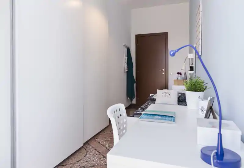 Camera da letto moderna e compatta con armadio bianco, scrivania e area notte — spazio luminoso e ordinato ideale per lavorare e rilassarsi.