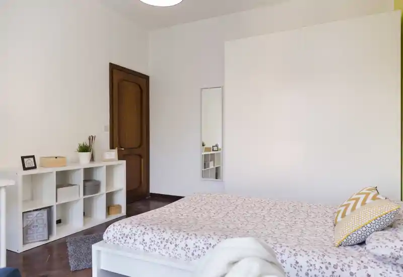 Camera da letto luminosa e ordinata con letto matrimoniale decorato, cuscini accoglienti e scaffalatura minimal—perfetta per foto di annunci.