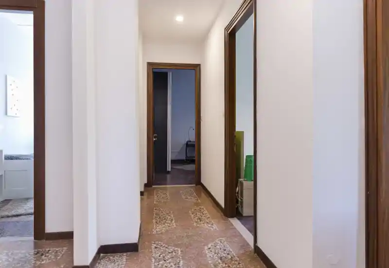 Bright, well-lit hallway/entrance with terrazzo floor and white walls, showing multiple doorways leading to adjoining rooms.