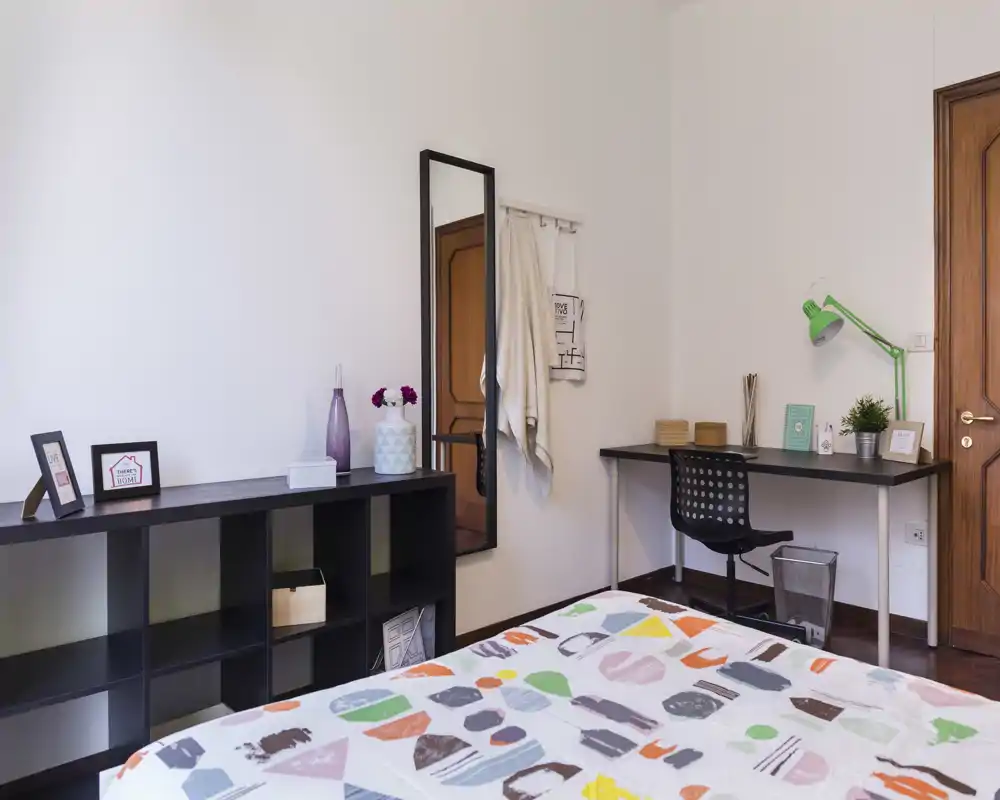 Bright, modern bedroom with a patterned duvet, desk workspace and decorative shelving — ideal for a single occupant or student.