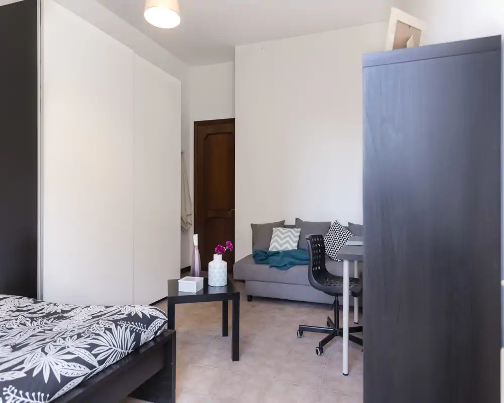 Dormitorio luminoso y ordenado con cama doble visible, armario grande y pequeña zona de estar con sofá y escritorio — ideal para una estancia cómoda.