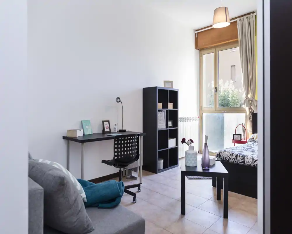 Dormitorio moderno y luminoso con cama individual, mesita y escritorio; ventana amplia y decoración cuidada, ideal para alquileres temporales o estudiantes.