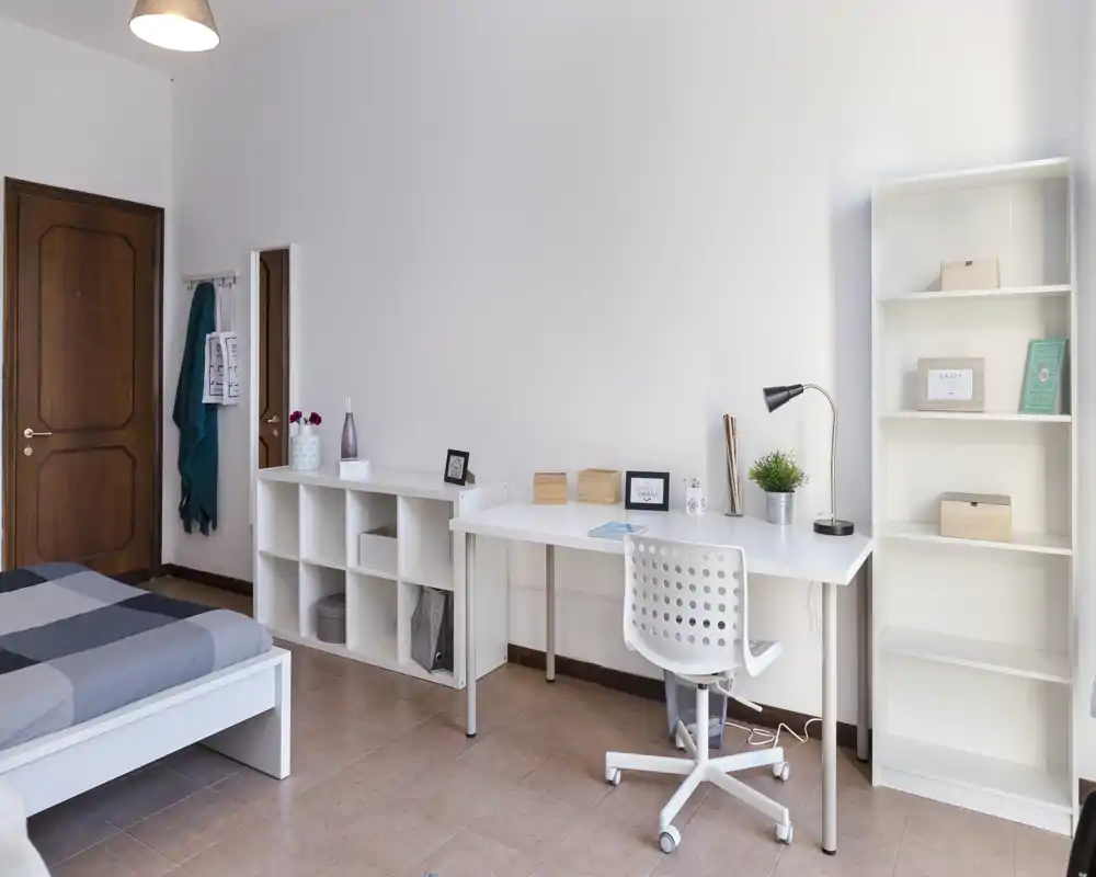 Chambre lumineuse et minimaliste avec lit blanc, bureau rangé et étagères — idéale pour étudiant ou télétravail.