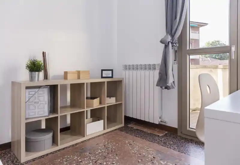 Bright, minimal living area with a low shelving unit, decorative boxes and a window letting in natural light — calm and tidy space ideal for a small sitting corner or study.