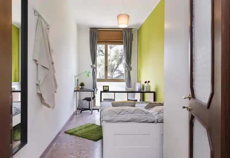 Chambre simple lumineuse et soignée avec lit, bureau près de la fenêtre, mur d'accent vert et textiles doux pour une ambiance chaleureuse.