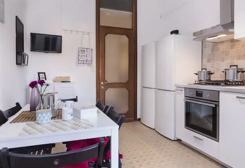 Bright, modern kitchen with a dining table set for use; white cabinets, built-in oven and fridge, and tasteful table decor create a welcoming cooking and eating space.