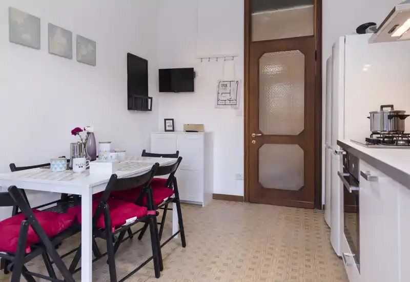 Bright, compact kitchen with a dining table set for four, red seat cushions, and modern white cabinets and appliances.