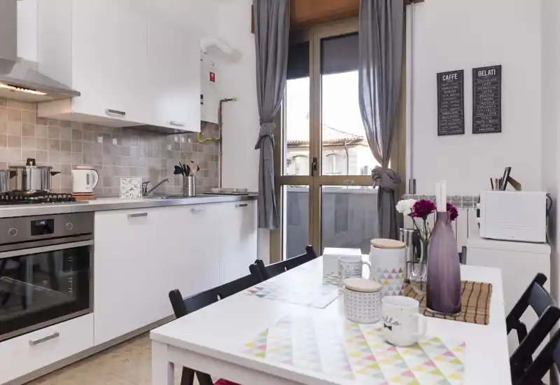 Bright, modern kitchen with white cabinets, built-in oven and a small dining table set with decorative placemats and a vase of flowers — ideal for cozy meals.