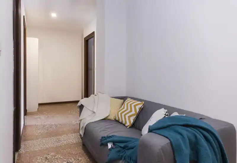 Compact living area with a grey sofa, colorful cushions and cozy throws; neutral walls and warm flooring create a calm, inviting corner perfect for relaxing.