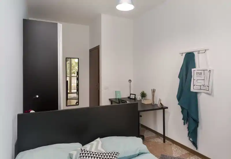 Chambre moderne et lumineuse avec lit bien visible, tête de lit épurée et textiles; petit bureau et armoire présents, espace de nuit pratique et chaleureux.