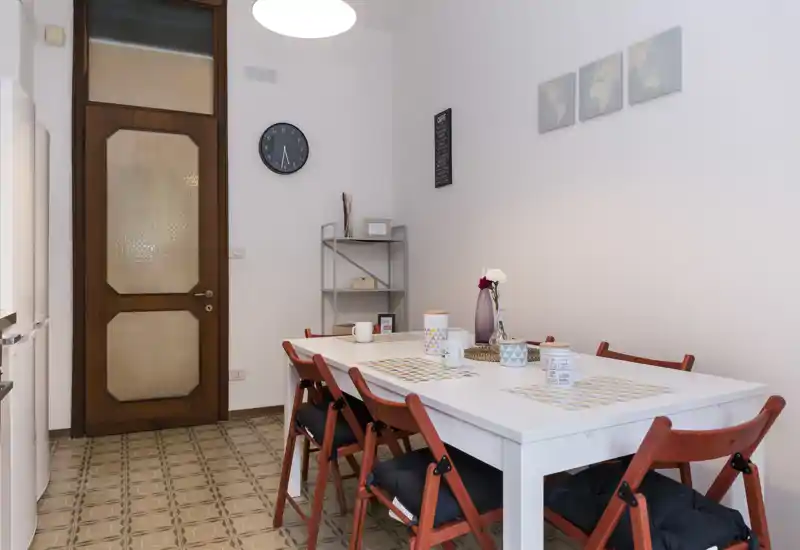 Bright, tidy dining area with a white table set with placemats, cups and a decorative vase; red folding chairs add a warm contrast to the neutral walls.