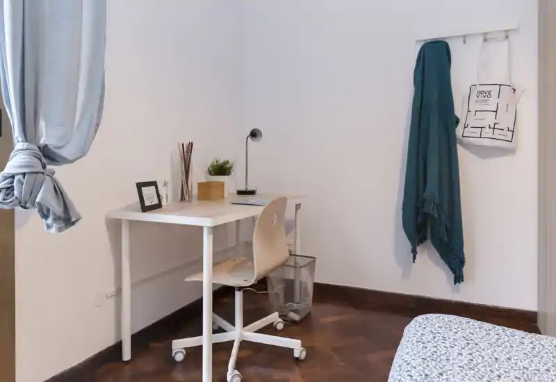 Cozy small bedroom corner with a simple desk and a partially visible bed; bright, tidy and suitable for a student or short-term stay.