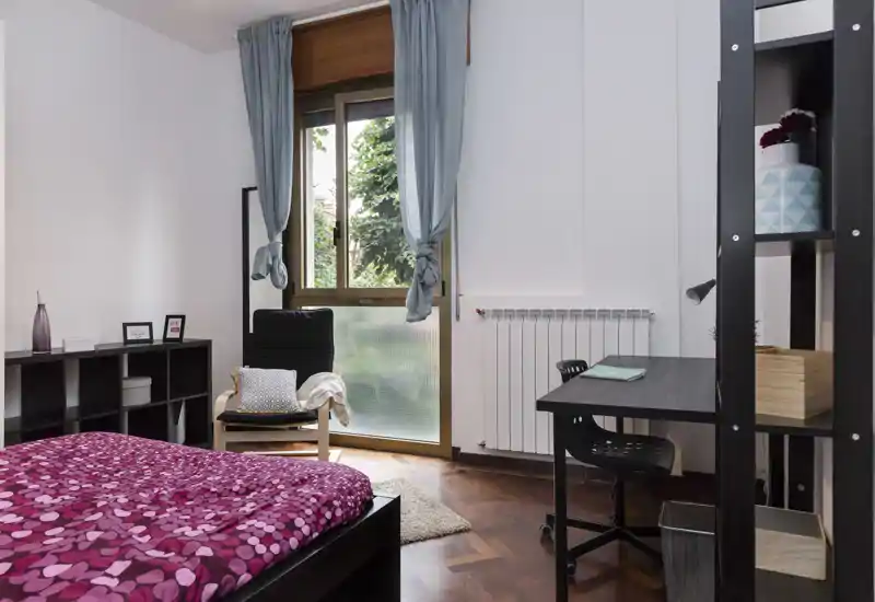Chambre lumineuse et chaleureuse avec lit double à couette imprimée, fauteuil près de la fenêtre et petit bureau — idéale pour étudiants ou professionnels.