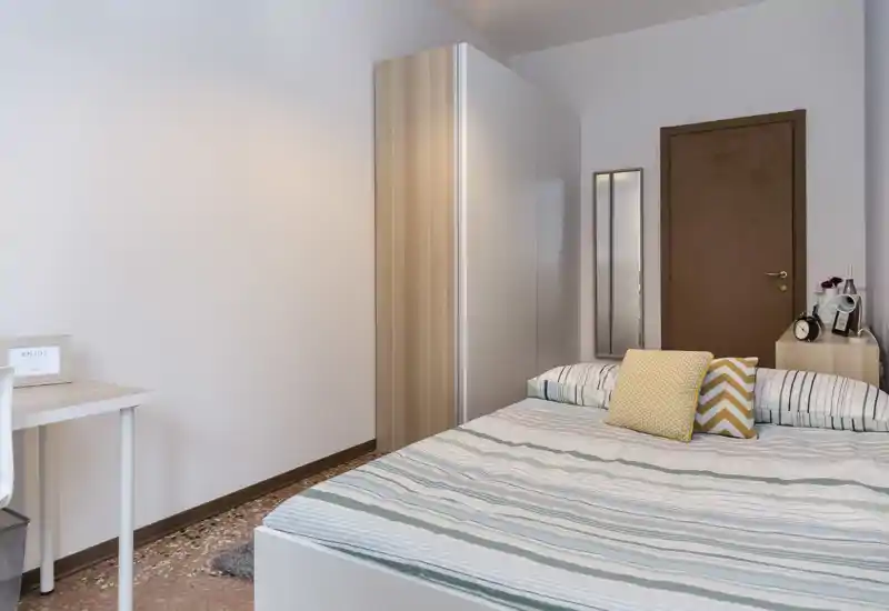 Chambre lumineuse et soignée avec lit double, coussins décoratifs, armoire et petit bureau — parfaite pour une annonce de location axée sur le confort et le rangement.