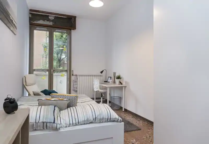 Chambre lumineuse et moderne avec un grand lit confortable, une literie rayée, un fauteuil près de la fenêtre et un petit bureau — idéale pour étudiant ou professionnel.