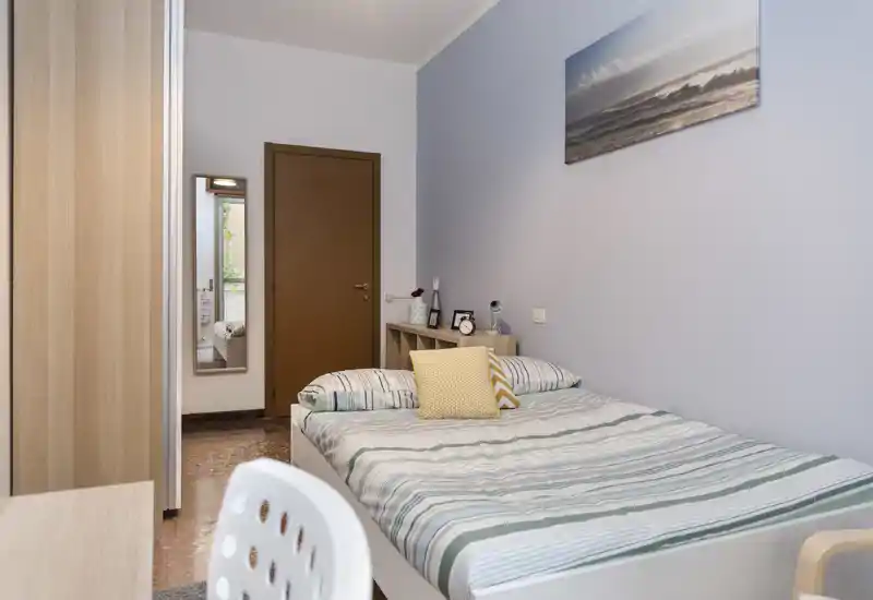 Chambre simple lumineuse et soignée avec lit rayé, coussins décoratifs et petite étagère de chevet — idéale pour un étudiant ou une personne seule.