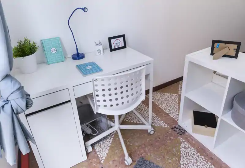 Small, tidy home-office corner with a white desk, perforated swivel chair, shelving unit and decorative accents. Bright and functional workspace suitable for a single occupant.