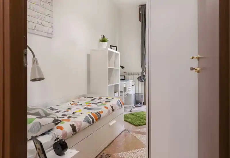 Chambre simple lumineuse et bien rangée avec couette colorée, tiroirs sous le lit et petit bureau près de la fenêtre — idéale pour étudiant ou personne seule.
