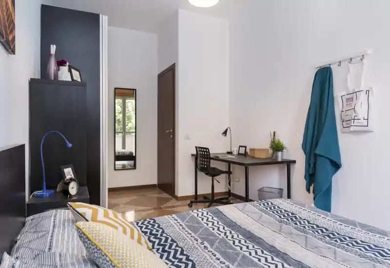 Dormitorio luminoso y bien presentado con cama doble estampada, mesita y un pequeño escritorio. La luz natural y los textiles crean un ambiente cálido, ideal para anuncios de alquiler.