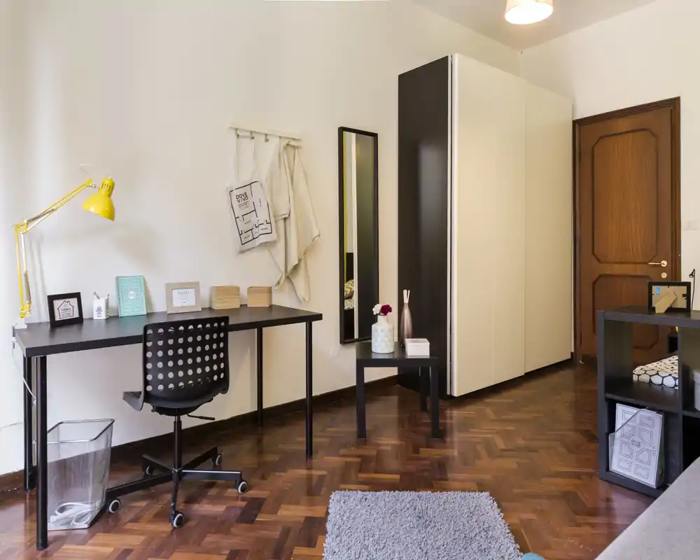 Angolo camera luminoso e ordinato con scrivania, armadio e zona relax — ideale per uno studente o per il lavoro da remoto.