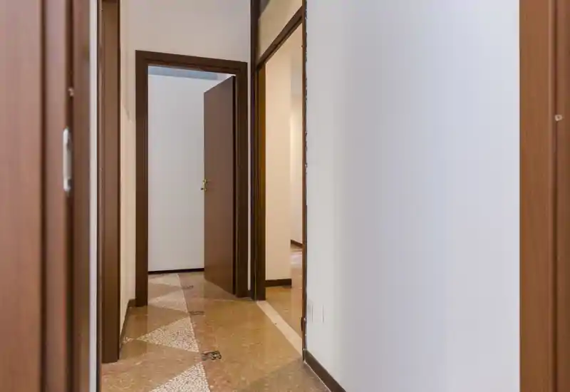 Bright, simple hallway with patterned terrazzo floor and wooden door frames leading to adjacent rooms — a clean, neutral entrance space.