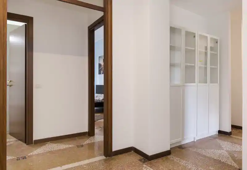 Bright entry hallway with tiled floor, white walls and a built-in glass-front cabinet; clear, well-lit space that leads to adjacent rooms.