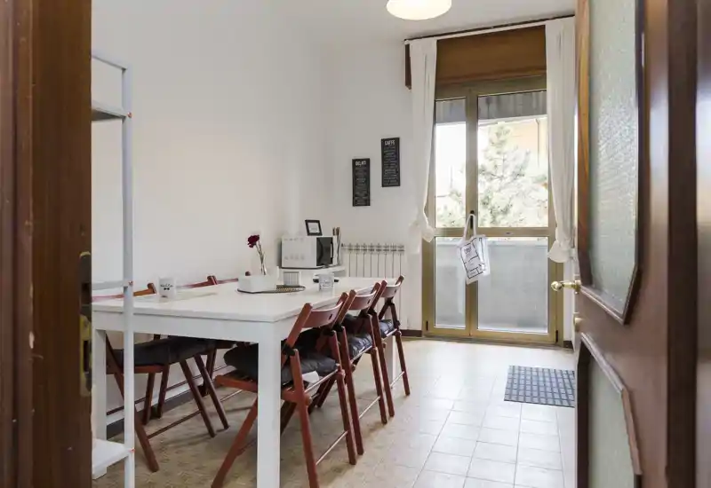 Bright, neatly staged dining area with a white table and several folding chairs, natural light from a large window/door and simple decorative touches for a welcoming feel.