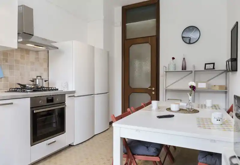 Bright, tidy kitchen with integrated oven, gas hob and a refrigerator, plus a dining table set with cushions and decorative items for a cozy mealtime.