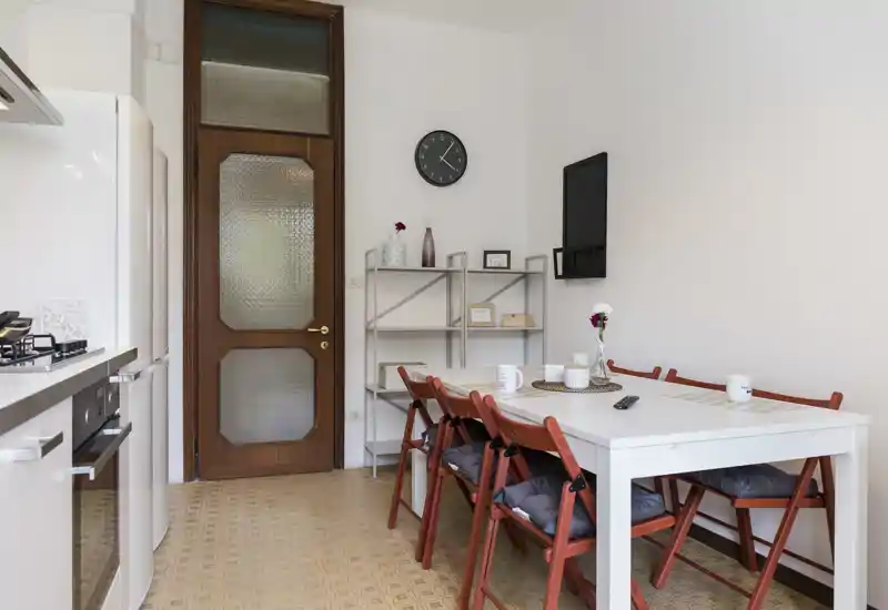 Bright, well-equipped kitchen with a white table and four cushioned chairs, gas stove and refrigerator visible — a clean, inviting dining corner ideal for casual meals.