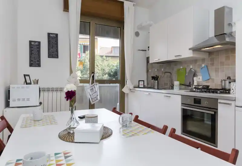Bright, modern kitchen with integrated oven and gas cooktop, a dining table set for casual meals, and a large window letting in natural light.