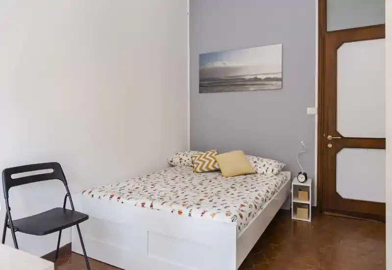 Camera da letto luminosa e ben curata con letto matrimoniale, biancheria a fantasia, cuscini decorativi e un piccolo comodino—perfetta per soggiorni confortevoli.