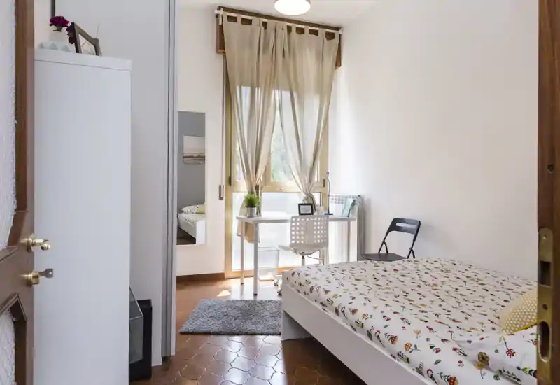 Camera singola luminosa e ben arredata con letto comodo, scrivania davanti alla finestra e dettagli decorativi curati — perfetta per un annuncio di affitto.