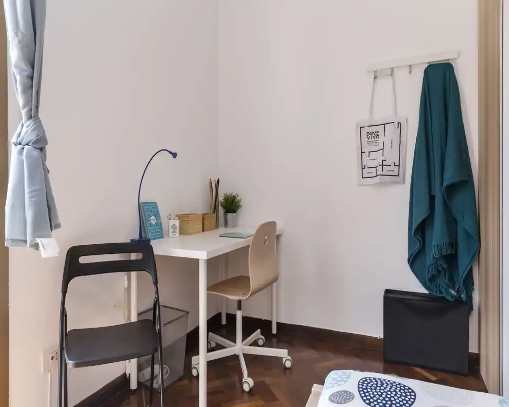 Coin chambre compact avec un petit bureau et une chaise à côté d'un lit partiellement visible ; propre, lumineux et simplement meublé — idéal pour une personne ou un étudiant.