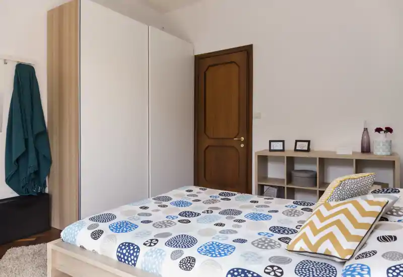 Chambre lumineuse et bien rangée avec un lit double à motifs, une armoire et des étagères — lignes épurées et lumière naturelle pour une atmosphère accueillante.