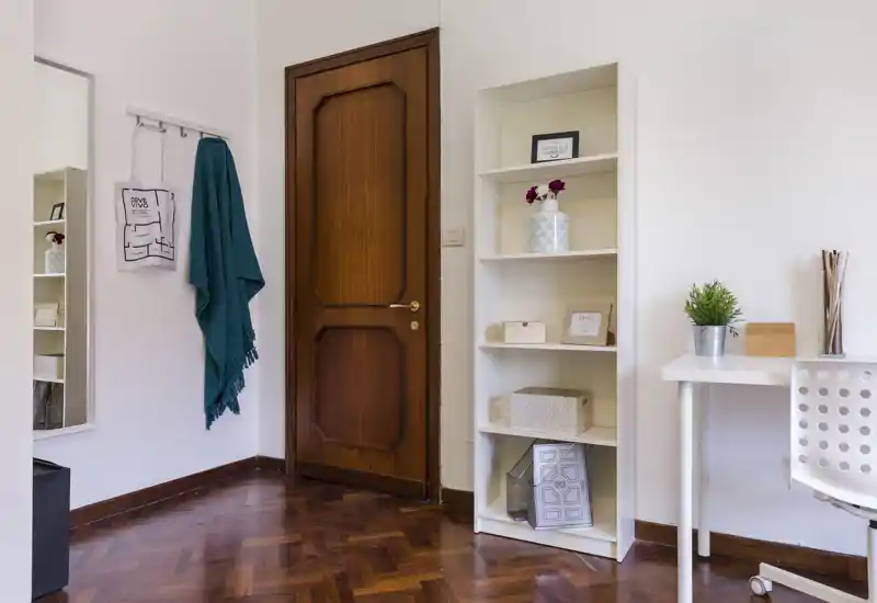 Bright, tidy living/working corner with a wooden door, shelving unit, desk and decorative accents — suitable for a compact urban apartment listing.