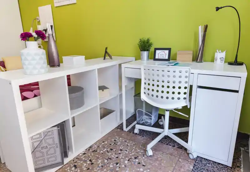 Bright, modern home-office corner with a white desk, perforated swivel chair and tidy shelving against a fresh green accent wall — ideal for productive stays.