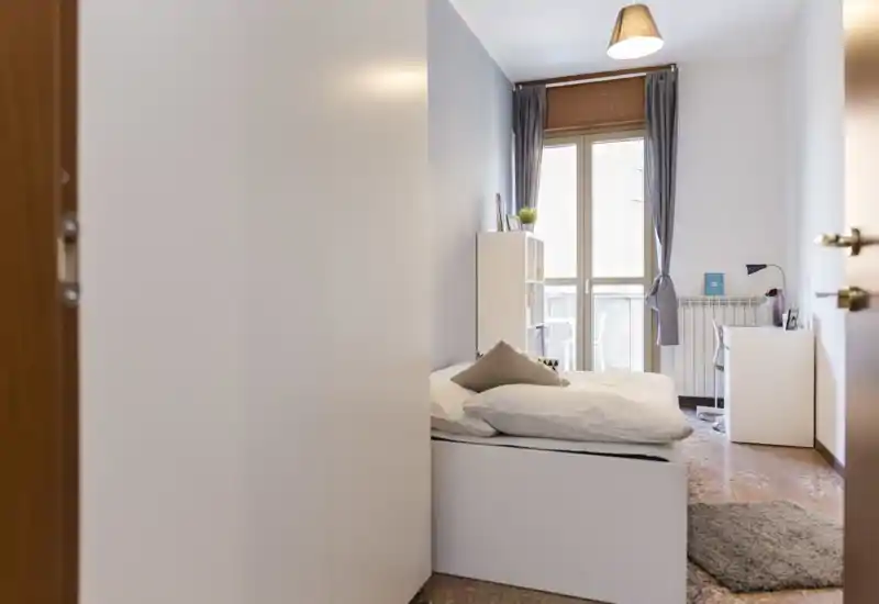 Bright, neatly staged bedroom with a single bed, soft textiles, desk and natural light from the balcony window — ideal for solo renters.
