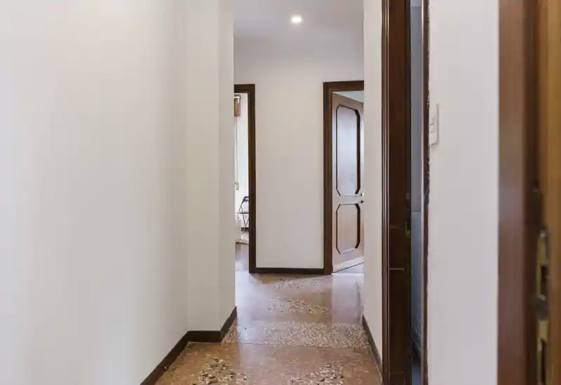 Bright hallway/entrance with terrazzo floor and wooden door frames; clean, neutral walls and overhead lighting create a welcoming first impression.