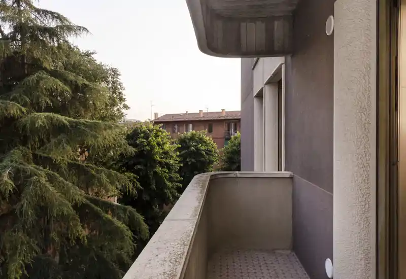 Sunny private balcony with concrete balustrade overlooking mature trees and neighboring buildings; ideal for morning coffee or adding small outdoor furniture.